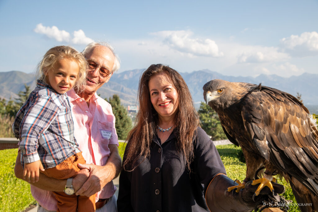 A woman with long dark hair in the middle of the frame poses with a Golden Eagle to her right and an older man holding a small child to the left